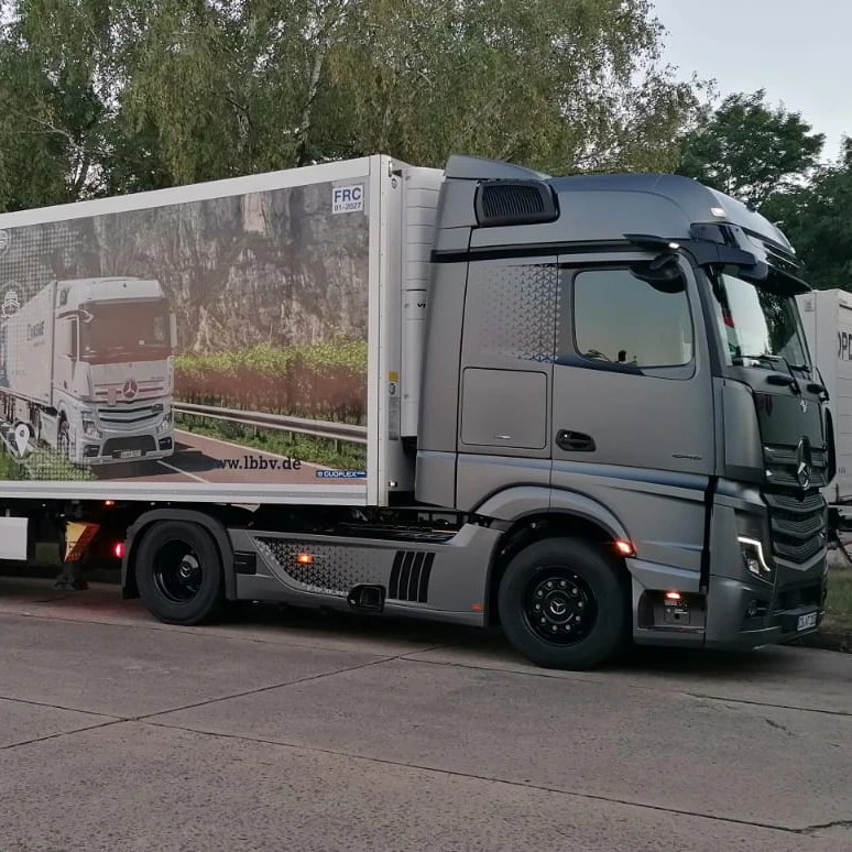 Grauer Lastwagen mit Werbebild auf der Ladefläche, geparkt auf einem Parkplatz.