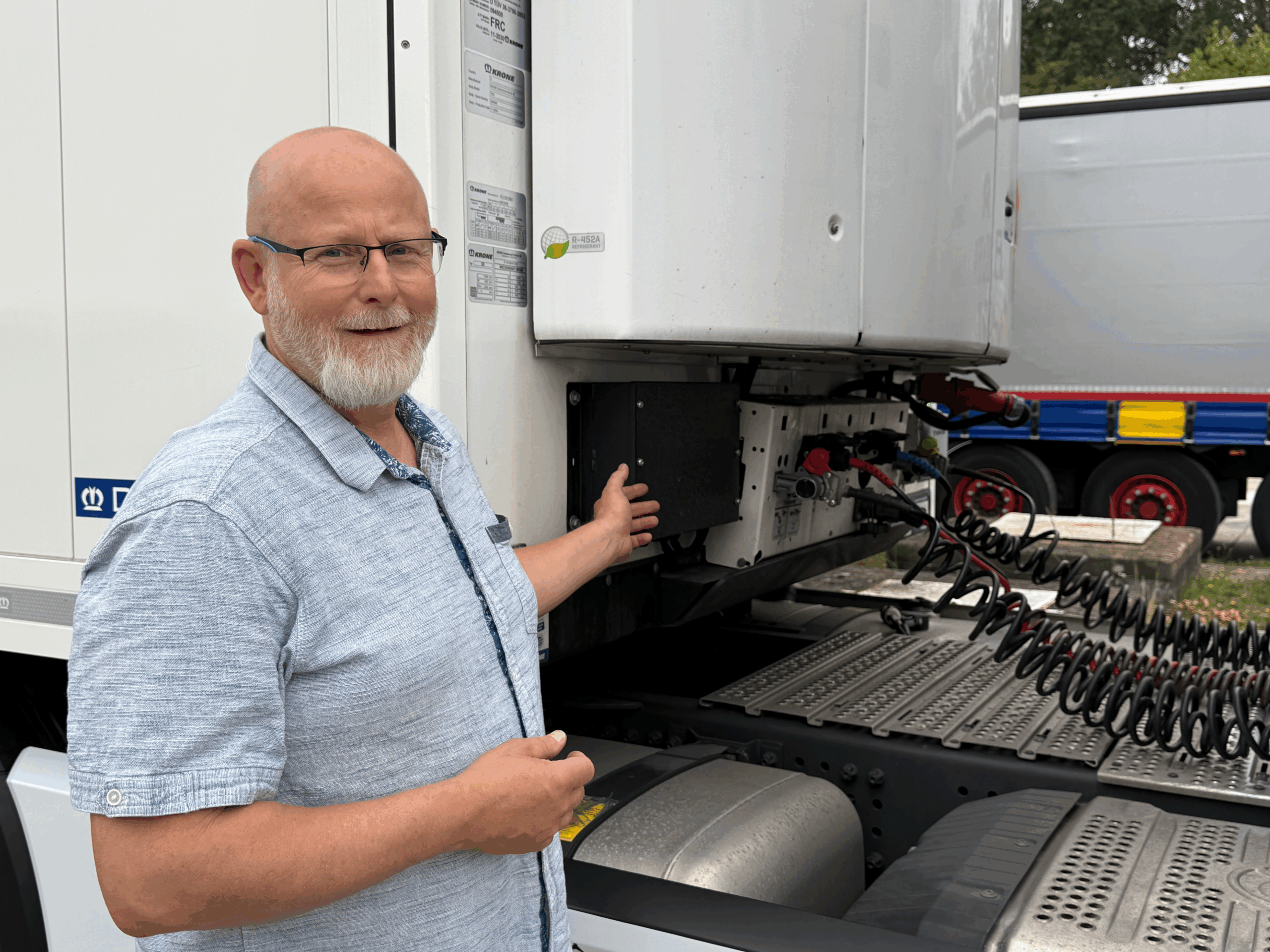 Mann zeigt auf die Rückseite eines LKWs mit angeschlossenen Kabeln.